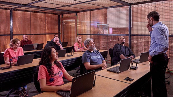 CSN students work at computers while an instructor speaks to the class in a lab.