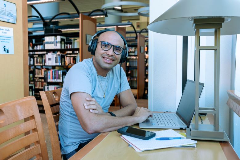 Man sitting with laptop wearing headphones in CSN library 