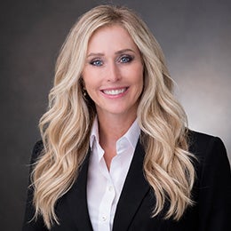 Professional headshot of Tina Russom wearing a black blazer and white shirt against a gray background.