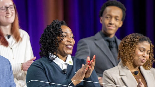 Group seated on stage, smiling and applauding during an event.