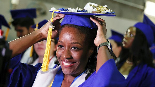 Graduate smiling while adjusting cap and gown tassel