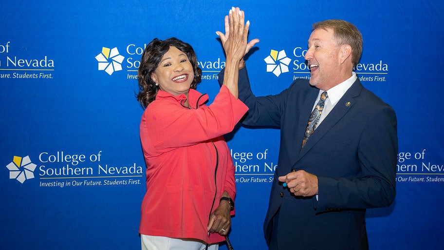 Two CSN leaders high-five in front of a College of Southern Nevada backdrop.
