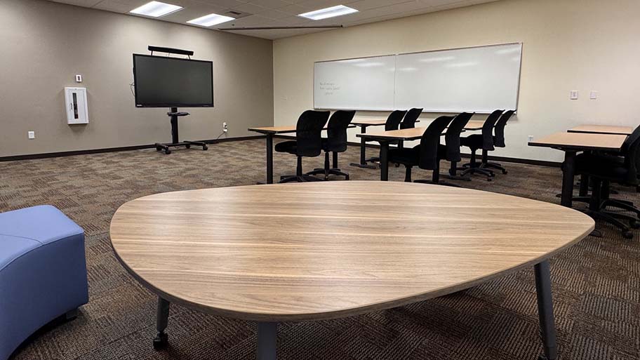 Faculty Center classroom with collaborative tables, chairs, a whiteboard and a digital display.