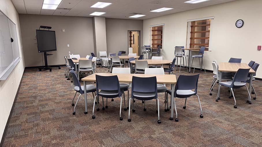 Faculty Center collaborative learning space with flexible tables, chairs, whiteboards and a digital display.