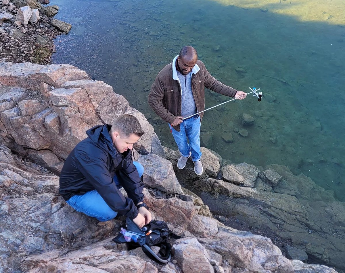 Two individuals taking water samples next to a lake.