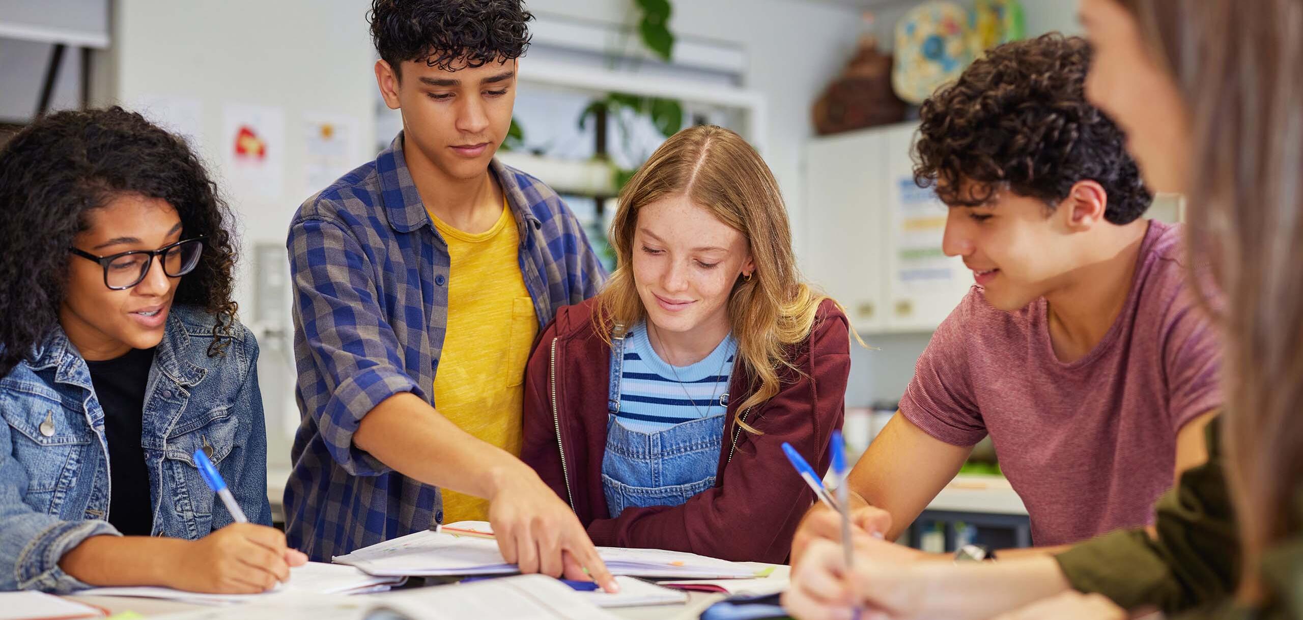 A group of students sitting together at a table, reviewing notes and studying collaboratively in a classroom setting.