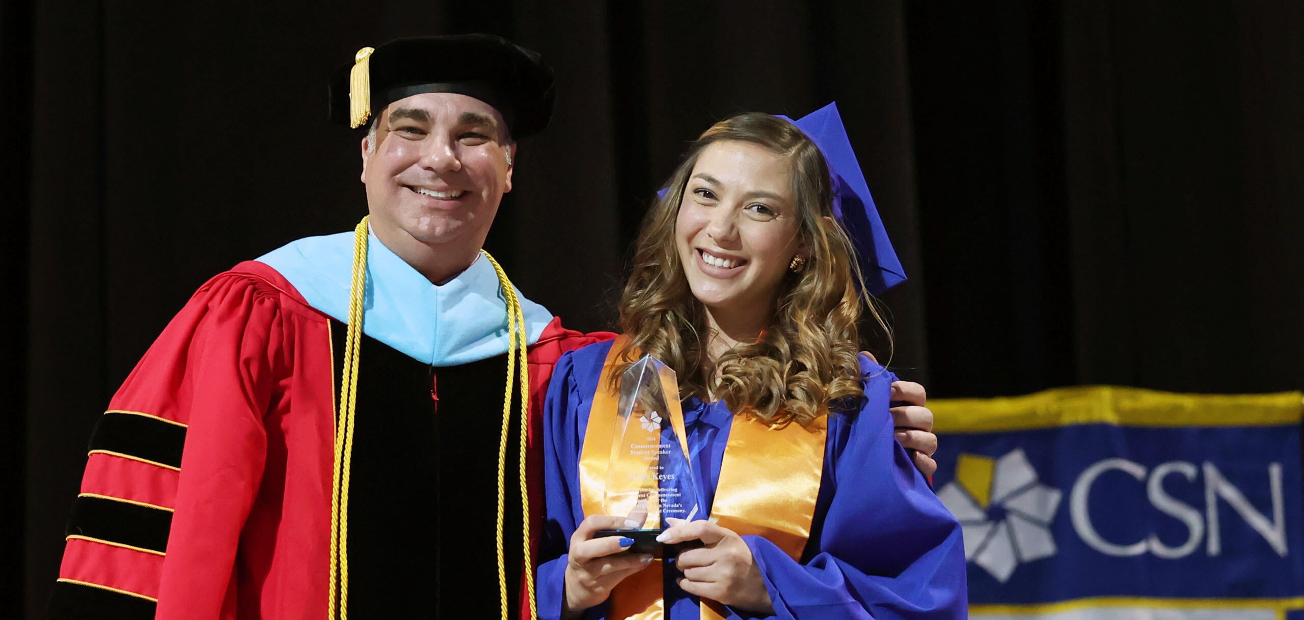 A CSN graduate receives the Commencement Student Speaker Award while standing with a faculty member during a commencement ceremony.