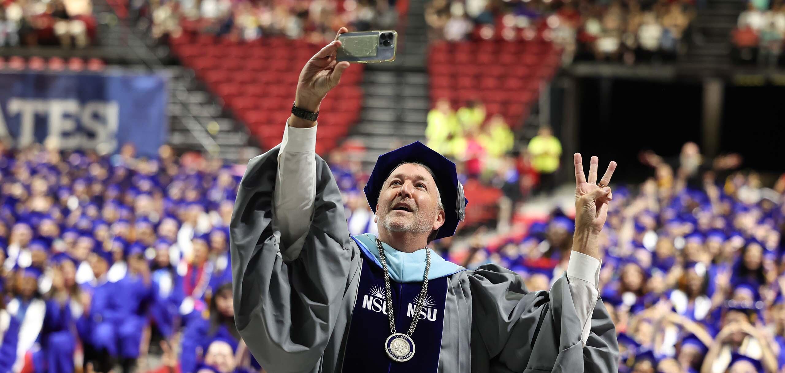 CSN President Dr. Stacy Klippenstein takes a selfie during commencement with graduates in the background.